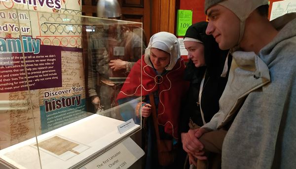 photo of people in historic costume looking at a small document in a display case.